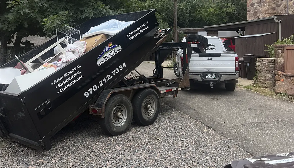 hauling away a full black dumpster rental from skyline roll off services, offering junk removal for homes and businesses