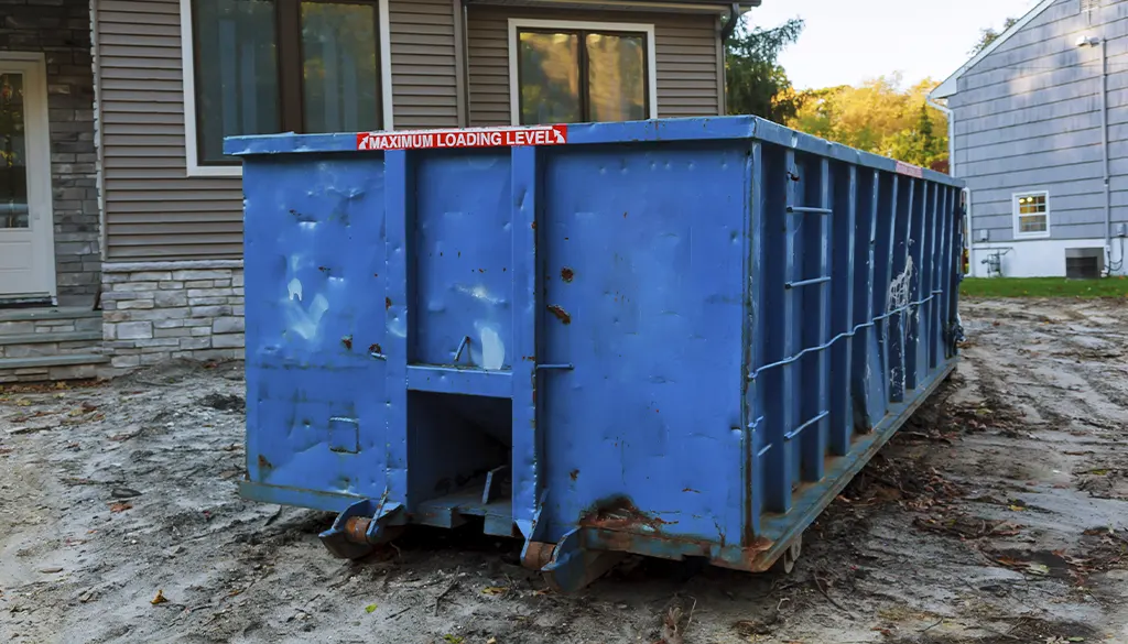 blue dumpster in mud in front of homes affected by flooding