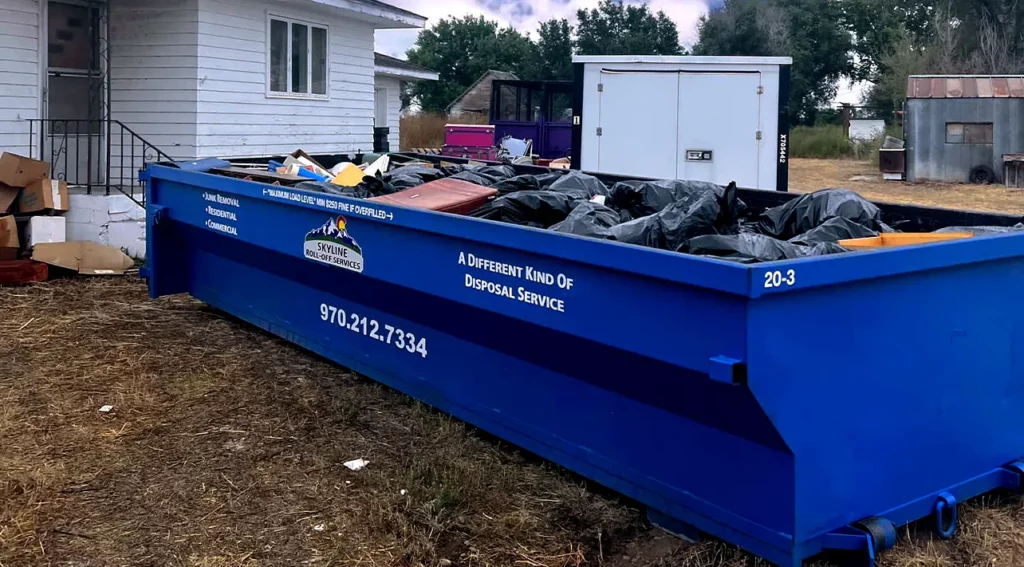 filled dumpster in front of home, with the logo "a different kind of disposal service" on the dumpster, including phone number to contact business, 970-212-7334